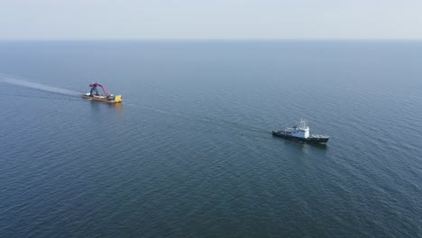 Tug-boat-VARMA-travelling-across-open-ocean-towing-yellow-barge-BIG-PARTNER-loaded-with-tracked-harbour-material-handling-cranes