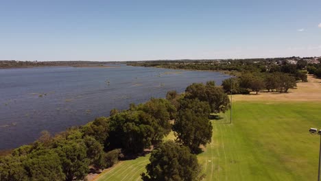 Aerial-footage-above-a-green-recreational-park-and-the-neighbouring-lake
