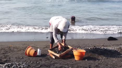 Trabajador-De-La-Construcción-Tradicional-Recoge-Piedras-Negras-De-La-Playa,-Bali-Asia-Indonesia