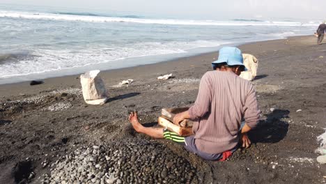 Balinesische-Frau-Sammelt-Schwarze-Steine-Vom-Strand,-Traditioneller-Arbeiter,-Küste-Von-Bali,-Indonesien