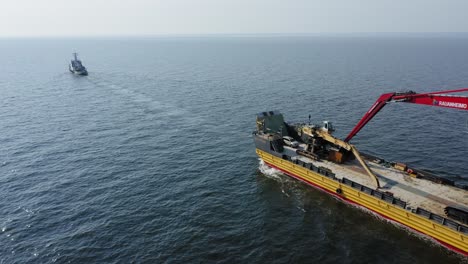 Tug-boat-VARMA-travelling-across-open-ocean-towing-yellow-barge-BIG-PARTNER-loaded-with-tracked-harbour-material-handling-cranes