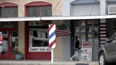 Woman-walking-downtown-Elgin,-Texas-with-an-American-flag-flying-in-the-wind