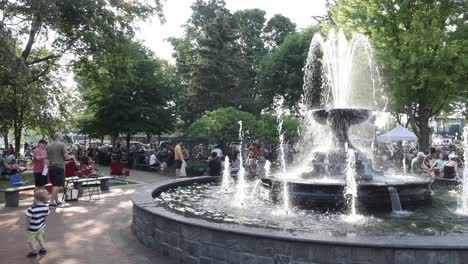 Fuente-De-Agua-Y-Gente-Reunida-En-Un-Concierto-De-Música-Al-Aire-Libre-En-El-Parque-Kellogg-En-Plymouth,-Michigan,-Con-Video-De-Cardán-Panorámico-De-Izquierda-A-Derecha