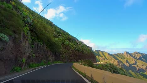 Driving-On-The-Beautiful-Island-Of-Tenerife-Surrounded-By-Green-Lush-Vegetation,-Tall-Mountain-Peaks-And-A-Blue-Ocean-In-The-Distance,-Curvy-Mountain-Roads,-Canary-Islands,-Spain