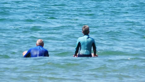 Healthy-active-retired-seniors-paddle-boarding-and-chatting-together-on-turquoise-welsh-waves
