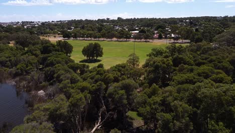 Aerial-view-above-green-park-with-trees-lining-lakeside-near-Joondalup,-Perth