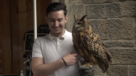 Witness-a-remarkable-scene-at-the-Royal-Mile-in-Edinburgh-as-a-man-holds-a-magnificent,-large-brown-owl,-creating-an-awe-inspiring-encounter-with-this-majestic-creature-of-nature