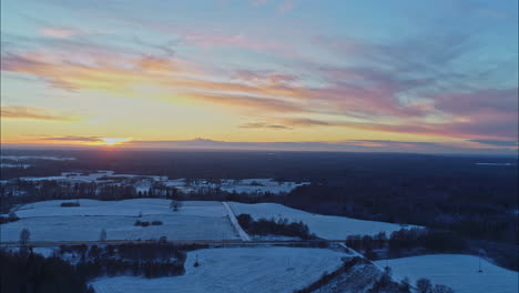 Aufsteigende-Panorama-Luftaufnahme-Einer-Winterlandschaft-Mit-Einem-Orangefarbenen-Sonnenuntergang