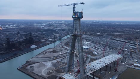 Tall-crane-in-construction-site-of-Gordie-Howe-international-bridge,-aerial-view