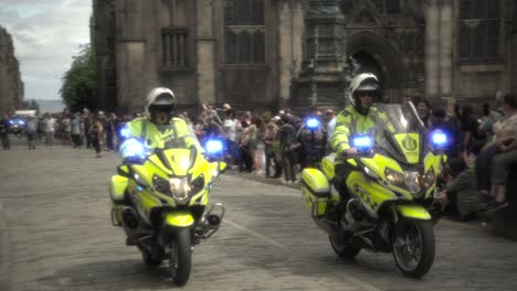Two-police-officers-on-bikes-slowly-ride-through-the-Royal-Mile,-providing-security-for-the-Pride-March