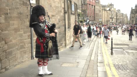 Immerse-yourself-in-the-vibrant-atmosphere-as-a-man-in-traditional-Scottish-attire-mesmerizes-the-crowd,-playing-the-bagpipes-at-the-iconic-Royal-Mile-in-Edinburgh