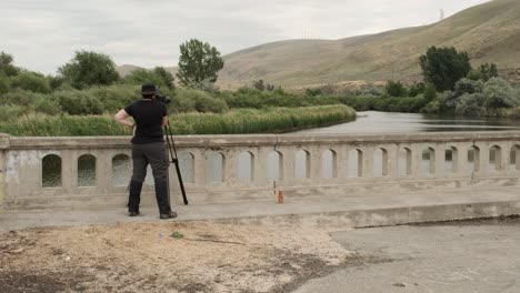 Female-photographer-with-large-camera-on-tripod-takes-photos-on-bridge