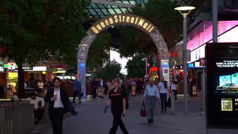 Menschen-Beim-Einkaufen-Und-Essen-Im-Belebten-Queen-Street-Mall-Bei-Nacht,-Statische-Aufnahme,-Die-Große-Menschenmengen-In-Der-Innenstadt-Von-Brisbane-Einfängt,-Mit-Leuchtendem-Wahrzeichen-Bogenschild-An-Der-Albert-Street-Im-Hintergrund