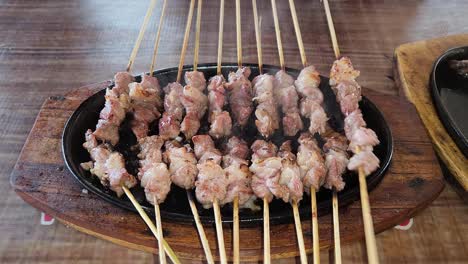 Fresh-goat-satay-cooking-on-heat-plate,-person-rotate-skewers,-close-up