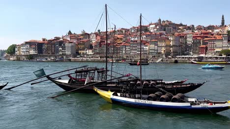 Panoramablick-Auf-Rabelo-Boote,-Ein-Traditionelles-Portugiesisches-Holzfrachtboot-Auf-Dem-Fluss-Douro-An-Sonnigen-Tagen---Altstadt-Mit-Historischen-Gebäuden-Im-Hintergrund