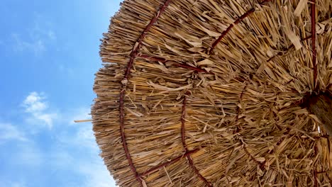 Close-up-on-part-of-wattled-straw-beach-umbrella-against-blue-sky-background