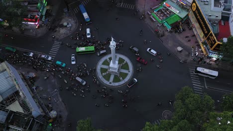 Traffic-roundabout-from-drone-flying-towards-center-of-intersection-with-large-white-monument-with-bus,-car-and-motorbike-traffic