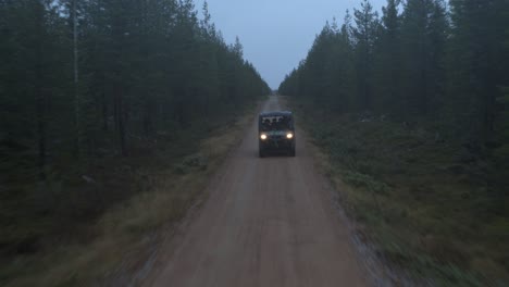 Side-by-side-UTV-races-through-dirt-road-in-foggy-pine-tree-forest-with-headlights-on
