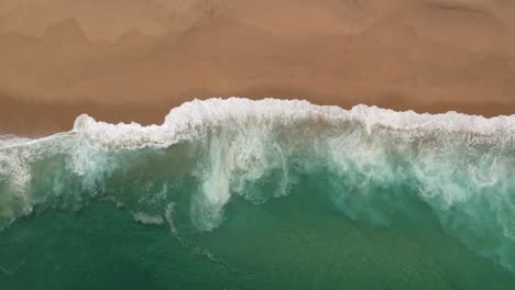 Top-down-view-of-Atlantic-Ocean-crashing-on-sandy-beach-in-Portugal