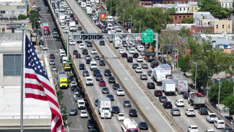 Cinematic-drone-shot-of-american-flag-on-flagpole-in-front-of-crowded-highway-in-Brooklyn-during-sunny-day---New-York-City,-USA---Tilt-up-wide-shot