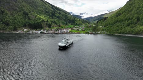 Ferryboat-Haroy-sailing-towards-camera-after-departing-idyllic-Eidsdal-village---Aerial-above-fjord-with-lush-valley-in-background---Norway