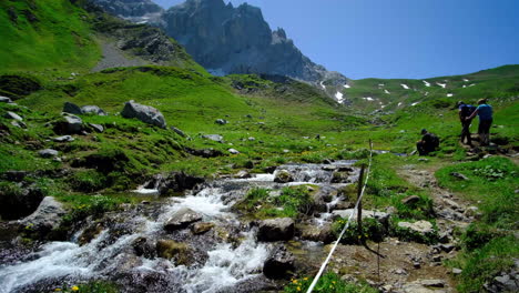 People-hike-up-towards-the-mountain,-a-beautiful-landscape-with-the-water-streaming