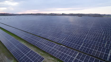 Aerial-panorama-of-solar-farm,-field-or-solar-power-plant-in-rows-with-photovoltaic-cells-in-panels-at-sunset