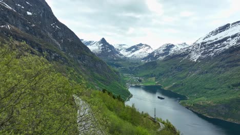 Geiranger-stunning-forward-moving-aerial-close-to-green-trees-with-famous-Unesco-listed-fjord-and-cruise-ship-seen-in-background---Norway