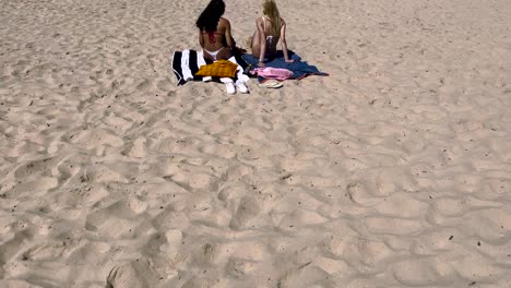 Dos-Hermosas-Mujeres-Jóvenes-Vistiendo-Bikinis-Paseando-Por-El-Borde-Del-Mar-En-Una-Playa-Tropical-Charlando-En-La-Playa-De-Caparica