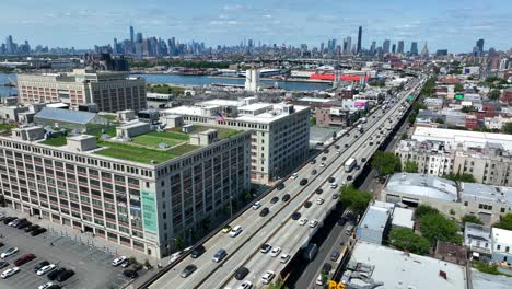 Aerial-establishing-shot-of-traffic-on-highway-in-Brooklyn-with-Skyline-of-Manhattan-in-background-during-sunny-day---Slow-forward-flyover