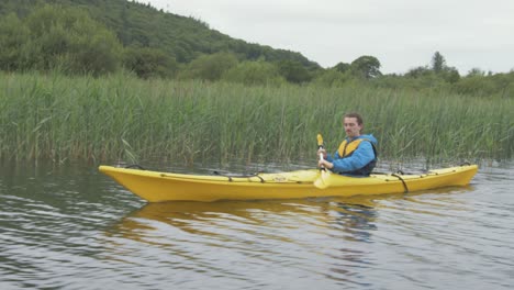 An-active-young-man-paddles-yellow-sea-kayak-along-the-river