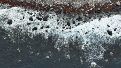 Blick-Von-Oben-Auf-Einen-Felsigen-Strand-Entlang-Der-Norwegischen-Atlantikküste-–-Wellen-Treffen-Langsam-Auf-Die-Küste,-Während-Sich-Die-Drohne-Langsam-Nach-Unten-Bewegt