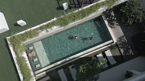 Rotating-aerial-rises-over-tourists-in-resort-courtyard-swimming-pool