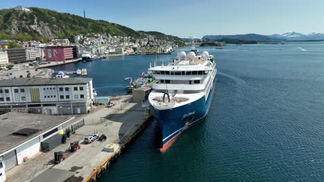 Cruise-ship-SH-Diana-moored-alongside-Alesund-Norway-during-a-beautiful-sunny-day---Aerial-around-bow-of-luxury-vessel-with-city-in-bckground