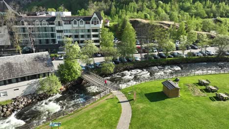 Tourist-walking-over-Geiranger-river-and-Hotel-Union-to-visit-the-Fjord-Center-on-the-other-side---Static-high-angle-aerial-view