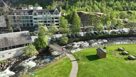 Tourist-Geht-über-Den-Fluss-Geiranger-Und-Das-Hotel-Union,-Um-Das-Fjordzentrum-Auf-Der-Anderen-Seite-Zu-Besuchen-–-Statische-Luftaufnahme-Aus-Der-Vogelperspektive