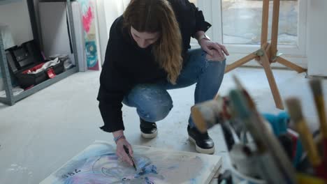 Female-artist-drawing-on-a-canvas-on-the-floor-of-a-home-studio