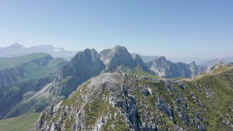Cinematic-aerial-of-group-of-climbers-on-top-of-a-high-mountain-summit-a-revealing-a-beautiful-valley