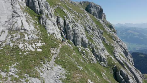 Drone-slowly-flying-towards-a-group-of-mountaineers-climbing-up-a-steep-and-rocky-ledge