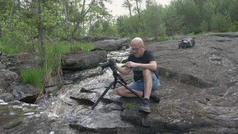 Nature-photographer-watching-his-camera-while-taking-long-exposure-photo-on-a-tripod-by-a-fresh-water-creek