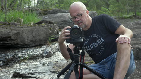 Fotógrafo-De-Naturaleza-Ajustando-Su-Cámara-Sobre-Un-Trípode-Junto-A-Un-Arroyo-De-Agua-Dulce