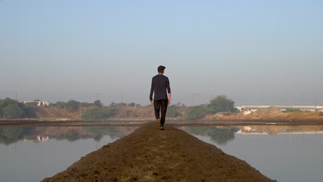 Hombre-Caminando-En-Un-Lago-Tranquilo-Con-Reflejos-De-Trenes-Locales-Que-Viajan-En-Ferrocarril-Indio-En-Mumbai---Toma-Amplia