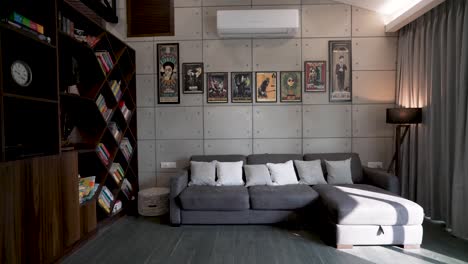 Graues-Sofa-In-Einem-Stilvollen-Wohnzimmer-Mit-Kunstwerken-An-Der-Wand-Und-Kreativem-Bücherregal-An-Der-Seite-–-Nach-Oben-Geneigte-Aufnahme