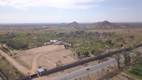 Drone-Flying-Away-From-The-Lush-Barren-Land-By-The-Road-In-Rajasthan,-India-On-A-Hot-Weather---aerial