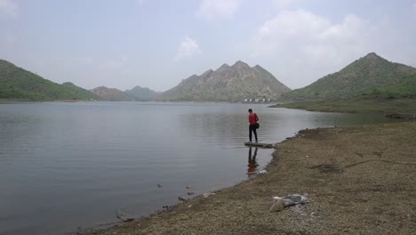 Männlicher-Tourist-Steht-In-Der-Nähe-Des-Wunderschönen-Udaipur-Sees-In-Rajasthan,-Indien---Weitwinkelaufnahme
