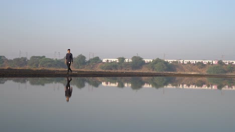 Man-Walking-On-The-Pathway-By-The-Lake-With-Reflections-On-The-Water-In-Mumbai,-India