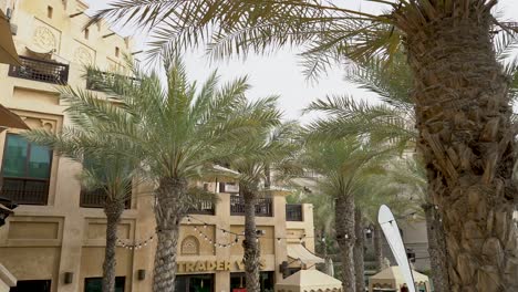 Blick-Auf-Den-Souk-Madinat-Jumeirah-Mit-Traditioneller-Arabischer-Architektur-In-Dubai,-Vereinigte-Arabische-Emirate-Mit-Palmen-Davor---Mittlere-Schwenkaufnahme