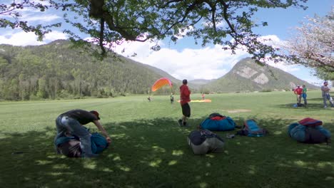 Paragliders-With-Their-Equipment-On-The-Lush-Field-In-Switzerland-On-A-Sunny-Day---wide-slowmo-shot