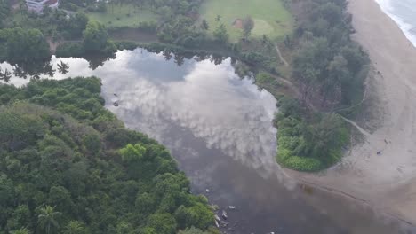 Ruhiges-Wasser-Des-Flusses-Mit-Wolkenspiegelung-In-Der-Nähe-Des-Lalit-Resorts-In-Rajbagh-Beach,-Canacona,-Süd-Goa,-Indien---Luftaufnahme-Einer-Drohne