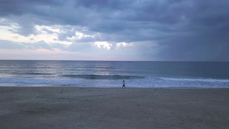 Eine-Einzelne-Person-Geht-Während-Der-Blauen-Stunde-Am-Sandstrand-Von-Rajbaga-In-Canacona,-Süd-Goa,-Indien,-Mit-Tosenden-Wellen-Spazieren